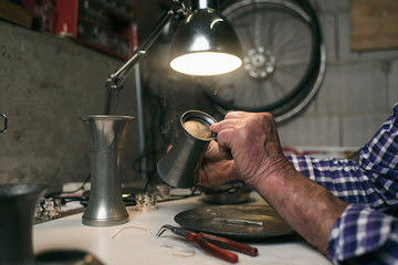 Hands of senior man inspecting antique tin vase