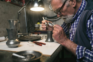 Man soldering old tin vase