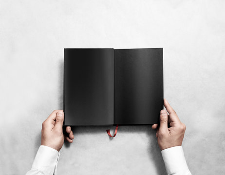 Hand holding blank opened book mock up with black pages. Person reading empty paperback mockup. Black notebook inside template. Publication design leafing man. Textbook spread with bookmark. - Powered by Adobe