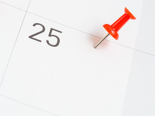 Red pin pinned on the 25th date of the month on calendar paper