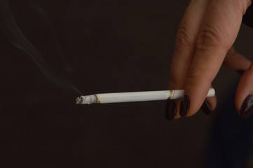 Woman's hand with dark polished nails holding a lit cigarette