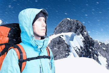 The mountaineer looks at the peak, standing against a winter mountain landscape.