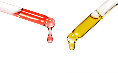 two pipettes with transparent colored liquids and oils drip
