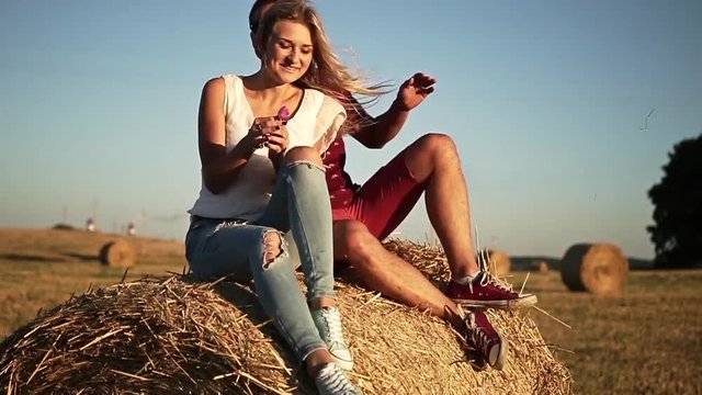 girl sitting on a haystack during sunset. the guy jumps on a haystack.