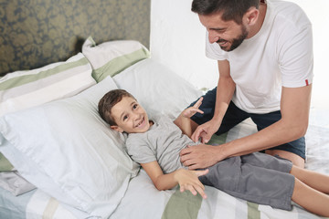 Father tickling his son on the bed