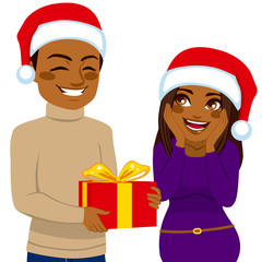 Cute African American man giving red present box to young surprised woman celebrating Christmas