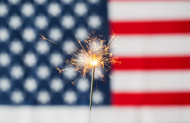 close up of sparkler burning over american flag