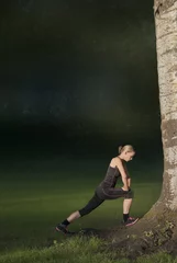 Foto op Plexiglas mooie jonge vrouw doet stretch oefeningen buiten in het park, vervaagde achtergrond voor copy-space © monicaclick