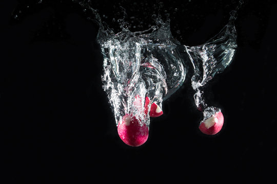 Fresh radish falling in water splash on black background