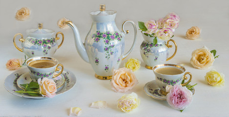 Beautifully decorated table for coffee: coffee pot, sugar bowl, milk jug, two cups of coffee and pink roses on a white background