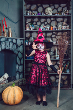 Girl in witch costume standing in halloween decorations with a broom in his hand