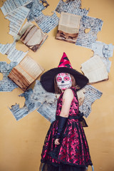 Girl in witch costume and makeup on her face standing  the background of yellow wall