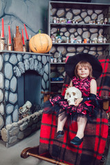 Girl in a witch costume sitting in  chair with  skull in his hands in in halloween decorations