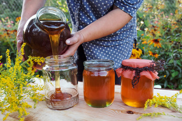 Honey spill from glass jar. Woman holding bottle of honey.