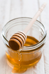 Honey dipper with honey in a jar on white wooden table

