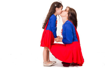 Mother and young daughter happily interacting together, both dressed in superman outfits with red skirts, all white studio background