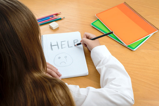 child abuse. A Horizontal image /poster covering the Social Issues of child abuse, by a schoolchild sat at a desk asking for help by a written message saying Help with a sad face .