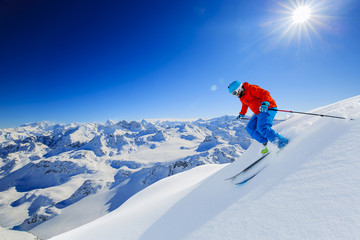 Skier skiing downhill in high mountains in fresh powder snow. Snow mountain range in background. Mt Fort Peak Alps region Switzerland.