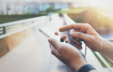 Hipster texting message on smartphone blank screen. Tourist using cellphone on bridge background close. Male hands holding gadget on blurred backdrop. Mockup copy space for message or design flare