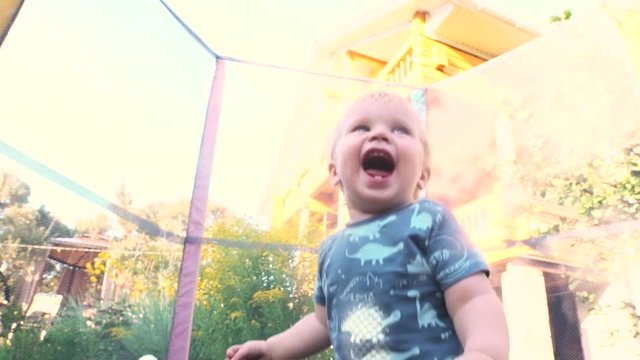 One year old baby boy jumping on trampoline. Happy little blond child with blue eyes jumping first time and having fun outdoor, slowmotion