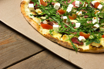 Appetizing pizza with ham, salami, arugula, cherry tomatoes, fetaksa, balsamic closeup on wooden background