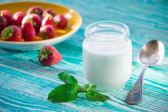 jar of yogurt and strawberry on turquoise colored wooden table