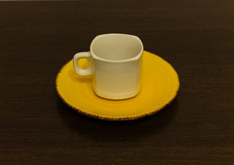 White mug on a yellow plate on a brown table