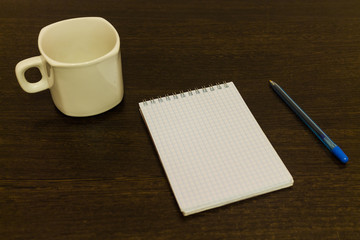 White notepad with a pen on a brown table with a cup of coffee