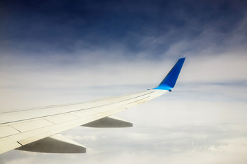 Fototapeta na wymiar Wing of an airplane flying above the clouds on blue sky background