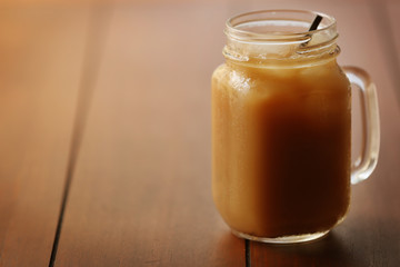 Iced coffee in glass jar with straw on brown wooden table