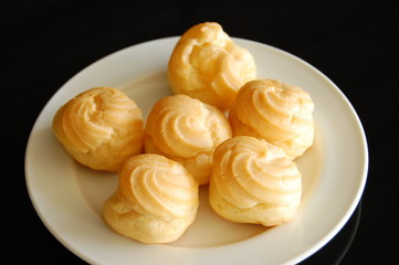 Eclairs or profiterole with chocolate and whipped cream preparing on baking sheet. Spreading...
