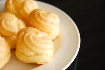 Eclairs or profiterole with chocolate and whipped cream preparing on baking sheet. Spreading chocolate on top of eclair with spoon. Traditional French dessert. Empty space for design text template.
