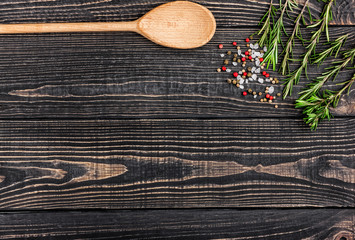 fresh rosemary, salt, pepper and a spoon on a black wooden backg