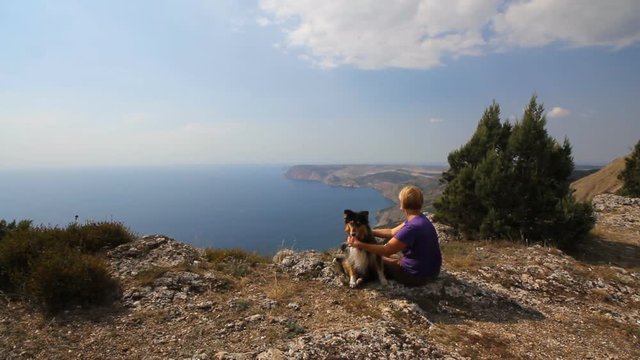 An elderly woman is resting on top of a mountain vacation with his funny big dog