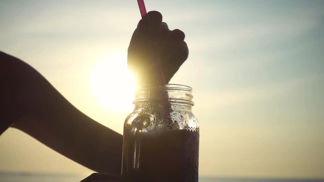 Girl's Hand Stirs a Cocktail in a Glass by Straw on the Sunset. Slow Motion