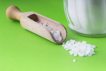 salt crystals with wooden spoon and glass salt shaker on green background