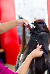 Fototapeta premium Hairstylist preparing a long brown hair in layers, a comb is helping her