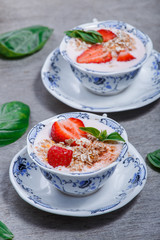 Healthy cereal with strawberries and yogurt decorate with mint in a ceramic bowls on wooden table, top view. Granola, muesli