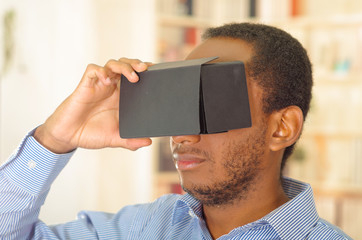 Man wearing blue shirt testing vitrual reality mobile device, holding glasses in front of eyes