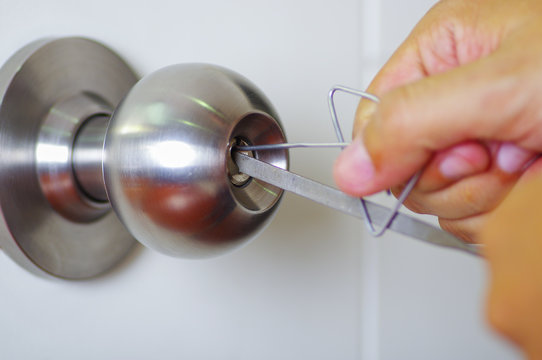 Closeup hands of locksmith using metal pick tools to open locked door
