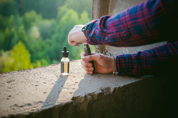 man in a plaid shirt and jeans runs vape juice electronic cigarette. He holds a mechanical mod with...