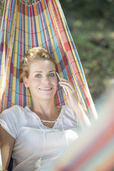 cheerful young woman using a phone in a hammock