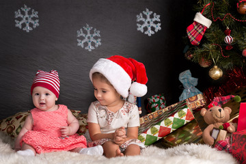 Cute baby girls sitting on rug with a Christmas presents