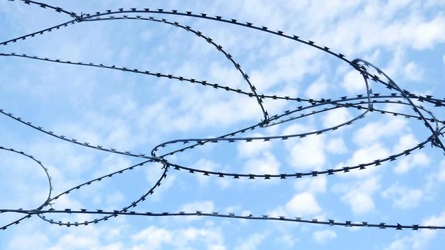 Barbed wire against the blue sky clouds prison video