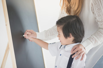 Cute Asian child writing on blackboard with
