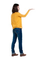 Back view of Beautiful business woman in yellow pulover looking at wall and Holds a hand up.  young brunette girl standing. Rear view people. Isolated over white background. 