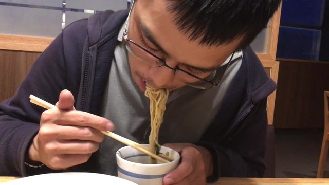 Asian young adult male wear coat jacket eating Japanese cold noodles soba served with soy sauce and wasabi