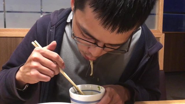 Asian young adult male wear coat jacket eating Japanese cold noodles soba served with soy sauce and wasabi