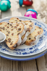 Traditional german Stollen with raisins and powdered sugar, on white and blue ceramic plate on wooden table. With espresso and jam. Traditional Christmas baking. Selective focus. Natural light