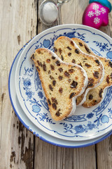 Traditional german Stollen with raisins and powdered sugar, on white and blue ceramic plate on wooden table. With espresso and jam. Traditional Christmas baking. Selective focus. Natural light